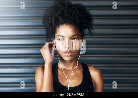 Einfach anschließen und losziehen. Aufnahme einer sportlichen jungen Frau, die beim Training vor grauem Hintergrund Musik hört. Stockfoto