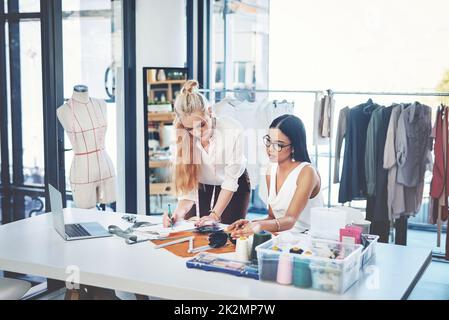 Unsere Kunden lieben es, wenn wir an Designs zusammenarbeiten. Aufnahme von zwei jungen Modedesignern, die in einem Workshop zusammenarbeiten. Stockfoto