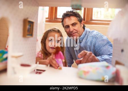 Gemeinsam kreativ und phantasievoll spielen. Ausgeschnittene Aufnahme eines Vaters und einer Tochter, die zu Hause mit einem Puppenhaus spielen. Stockfoto