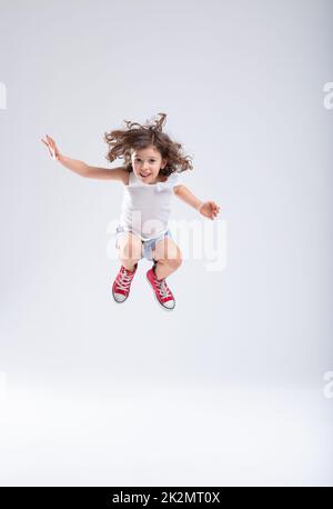 Ein energiegeladenes kleines Mädchen, das hoch in die Luft springt Stockfoto