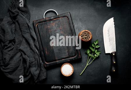 Leeres Holzschneidebrett, Salz, Pfeffer und Messer auf schwarzem Holztisch, Draufsicht Stockfoto