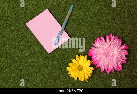 Leeres Notizpapier auf grünem Grashintergrund mit bunten Blumen Stockfoto