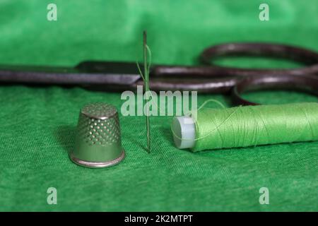 Spule aus grünem Faden, Nimble und Nadel auf grünem Stoff Stockfoto
