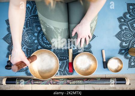 Yoga-Konzept, Meditation und Klangtherapie. Schöne junge kaukasische Frau, umgeben von tibetischen Klangschalen und Instrumenten aus Kupfer. Stockfoto