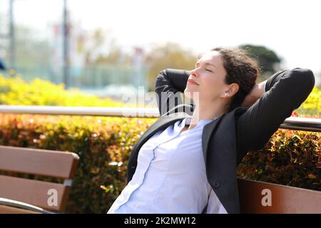 Eine entspannte Geschäftsfrau, die sich auf einer Bank in einem Park ausruht Stockfoto