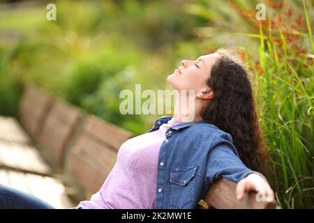 Eine Frau, die sich entspannt atmet und auf einer Bank in einem Park sitzt Stockfoto