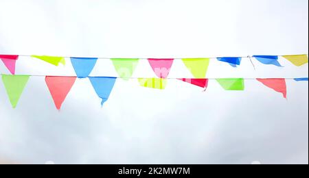 Bunte dreieckige Flaggen hängen an einer Schnur und flattern im Wind gegen einen wolkigen, wolkigen Himmel Stockfoto