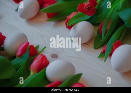 Rosafarbene Tulpen mit grünen Blättern liegen horizontal mit weißen Ostereiern vermischt und lassen diagonal freien Platz Stockfoto