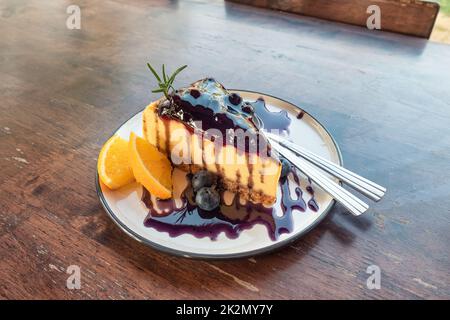 Heidelbeer-Käsekuchen mit Keks, Marmelade und Orange in Schale auf dem Tisch Stockfoto
