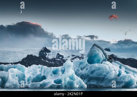 Wunderschöne Landschaft mit blauem Eisberg und dem Mond in der Jokulsarlon Gletscherlagune in der Abenddämmerung im Sommer im Vatnajokull Nationalpark, Island Stockfoto