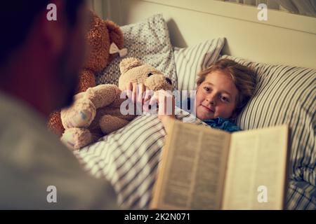 Magische Geschichten, um einige sweetdreams zu entfachen. Eine kleine Aufnahme eines Vaters, der seiner kleinen Tochter zu Hause eine Geschichte zur Schlafenszeit vorliest. Stockfoto
