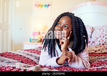 Sein Morgen, darüber nachzudenken, was heute zu tun ist. Aufnahme eines entzückenden kleinen Mädchens, das in ihrem Schlafzimmer auf ihrem Bett chillt. Stockfoto