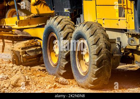 Straßengrader, der auf der Baustelle für die Wartung und den Bau von Schmutz- und Schotterstraßen arbeitet. Gelber Motorgrader. Schwere Maschinen und Baumaschinen zum Planieren von Straßen. Planiermaschine. Stockfoto