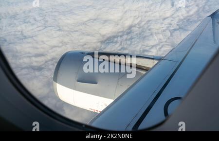 Blick von innen durch ein Ebenenfenster über weiße Wolken. Fensteransicht des Flugzeugs sieht einen Flugzeugmotor. Ein Flugzeug, das am Himmel fliegt. Gewerblicher Flug. Auslandsreisen nach COvid-19. Stockfoto