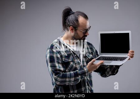 Ein Mann mit Pferdeschwanz und Brille, der einen Laptop in der Hand hat Stockfoto