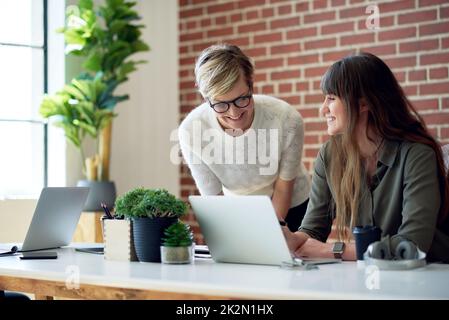 Zwei Frauen aus der Geschäftswelt, die im Büro mit einem Laptop arbeiten, teilen ihre Ideen mit Kollegen auf dem Bildschirm Stockfoto