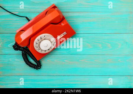 Altes, orangefarbenes Drehwahltelefon auf blauem Holzhintergrund Stockfoto