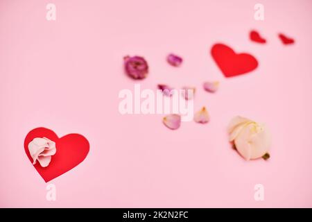 Rote Papierherzen und Rosenblätter auf rosa Hintergrund. Stockfoto