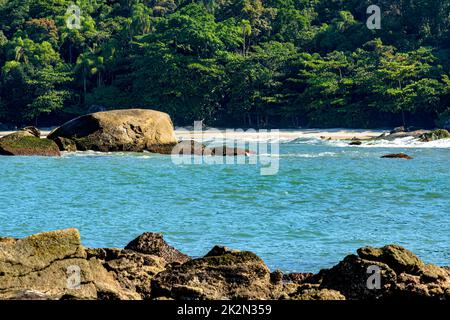 Verlassener Strand mit farbenfrohem und transparentem Wasser zwischen Felsen, Bergen und Regenwald Stockfoto