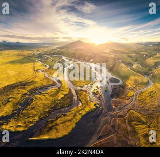 Luftaufnahme des Sonnenuntergangs über vulkanischen Bergen und abstrakten Gletscherflüssen, die durch Moosfelder im isländischen Hochland fließen Stockfoto