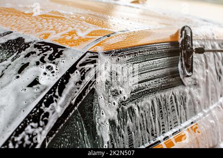 Gelbe Auto in Self-Service-Autowaschanlage gewaschen, Pinsel, Anschläge in white Shampoo und Schaum auf Seite Fenster Glas. Stockfoto