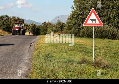 Liptovsky Hradok, Slowakei - 22.. August 2018: Achtung Kühe überqueren Schild, neben der Straße mit kommendem Traktor, Landschaft, Hügel und Berge in der Ferne. Stockfoto