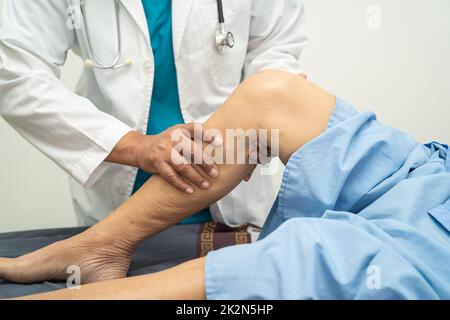 Asiatischer Arzt Physiotherapeut Untersuchung, Massage und Behandlung von Knie und Bein von älteren Patienten in der orthopädischen medizinischen Klinik Krankenschwester Krankenhaus. Stockfoto