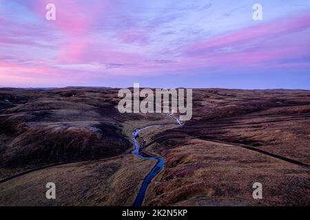 Luftaufnahme des farbenfrohen Himmels über dem Moos-Lavafeld mit dem Fluss, der im isländischen Hochland in der Wildnis bei Sonnenuntergang in Island fließt Stockfoto