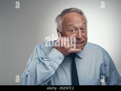 Vergessen Sie nicht, mir einen Ring zu geben. Aufnahme eines älteren Geschäftsmannes, der allein vor grauem Studiohintergrund steht und eine Handbewegung mit dem Handy macht. Stockfoto