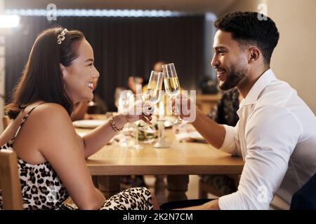 Ich bin so froh, dass wir uns in diesem Jahr getroffen haben. Aufnahme eines glücklichen jungen Paares, das während einer Silvestergarty zusammen sitzt und mit Champagner rösten kann. Stockfoto