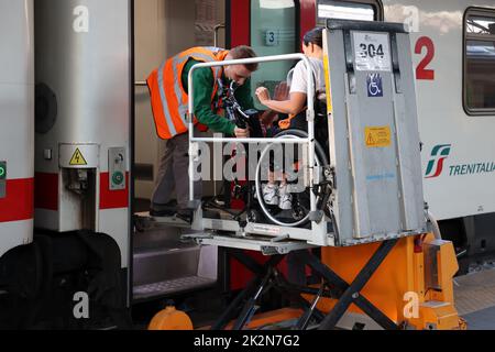 Neapel, Italien - 21. September 2022: Im Bahnhof wird ein behinderter Fahrgast im Rollstuhl mit einem speziellen für auf dem Zugwagen transportiert Stockfoto