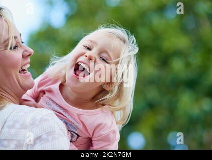 Es gibt nichts Süsseres als ein Kinderlachen. Aufnahme eines niedlichen kleinen Mädchens, das lacht, während sie von ihrer Mutter draußen gehalten wird. Stockfoto