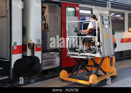 Neapel, Italien - 21. September 2022: Im Bahnhof wird ein behinderter Fahrgast im Rollstuhl mit einem speziellen für auf dem Zugwagen transportiert Stockfoto