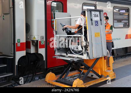 Neapel, Italien - 21. September 2022: Im Bahnhof wird ein behinderter Fahrgast im Rollstuhl mit einem speziellen für auf dem Zugwagen transportiert Stockfoto