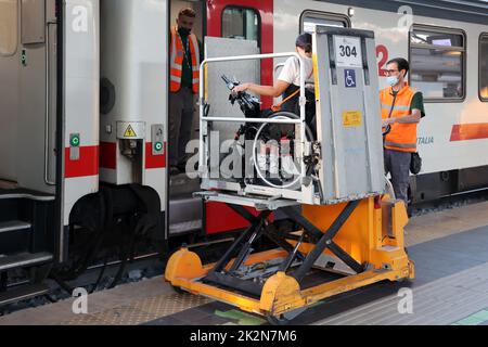 Neapel, Italien - 21. September 2022: Im Bahnhof wird ein behinderter Fahrgast im Rollstuhl mit einem speziellen für auf dem Zugwagen transportiert Stockfoto
