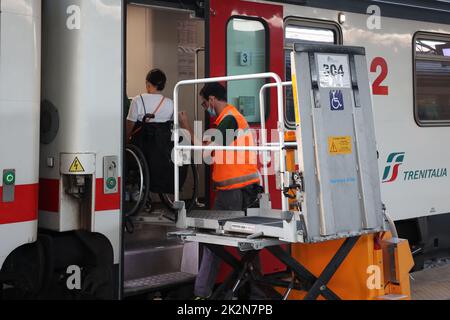 Neapel, Italien - 21. September 2022: Im Bahnhof wird ein behinderter Fahrgast im Rollstuhl mit einem speziellen für auf dem Zugwagen transportiert Stockfoto
