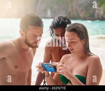 Erinnerungen machen, während sie jung sind. Ausgeschnittene Aufnahme von drei jungen Freunden, die Fotos am Strand angeschaut haben. Stockfoto