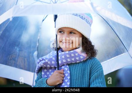 Der Regen war schon immer mein Favorit. Aufnahme eines entzückenden kleinen Mädchens, das allein draußen steht und einen Regenschirm hält. Stockfoto