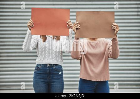 Heben Sie Ihre Stimme. Eine kurze Aufnahme von zwei nicht erkennbaren Frauen, die während einer politischen Kundgebung Schilder hielten. Stockfoto