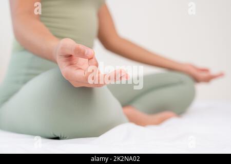 Frau, die Meditation auf dem Bett praktiziert. Yoga-Atmung mit Ardha Padmasana-Training. Stockfoto