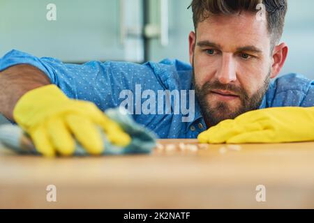 Die Hausarbeit wie ein Hochschuder erledigen. Aufnahme eines Mannes, der Gummihandschuhe trägt, während er zu Hause einen Tisch abwischt. Stockfoto