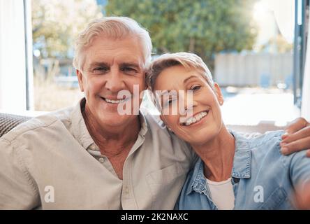 Seniorenportrait Entspannen Sie sich auf einem Sofa gemeinsam in ihrem Wohnzimmer oder Sommerferienhaus. Lächeln, Zuneigung und Liebe mit Stockfoto