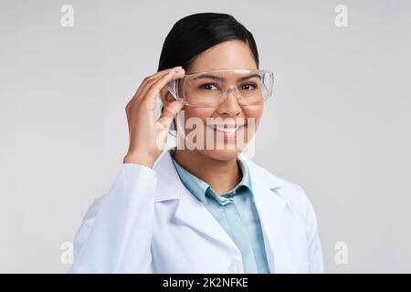 Bereit für die Arbeit. Beschnittenes Porträt einer attraktiven jungen Wissenschaftlerin, die im Studio vor grauem Hintergrund eine Brille trägt. Stockfoto