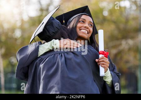 Wir haben es getan. Kurze Aufnahme einer attraktiven jungen Studentin, die ihre Freundin umarmte, während sie am Abschlusstag feierte. Stockfoto