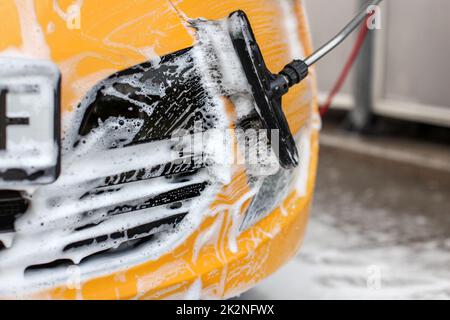 Gelbe Auto vorne in selbst gewaschen dienen Carwash, weiß Shampoo Schaum kontrastierenden mit schwarzer Maske und Bürste. Stockfoto