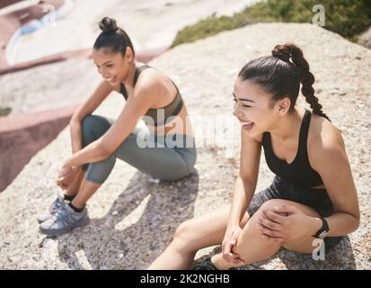 Eine tolle Zeit während ihrer Aufwärmphase zu haben. High-Angle-Aufnahme zweier attraktiver sportlicher junger Frauen, die eine Pause vom Training am Strand einlegen. Stockfoto