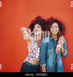 Beste Freunde machen die glücklichen Zeiten noch glücklicher. Aufnahme von zwei jungen Freunden, die vor einem roten Hintergrund posieren. Stockfoto