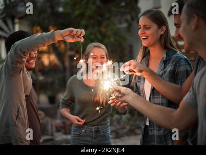 Wer wusste, dass Funkeln dieser Spaß sein könnte. Aufnahme einer Gruppe von fröhlichen jungen Freunden, die sich nachts mit Wunderkerzen amüsieren. Stockfoto