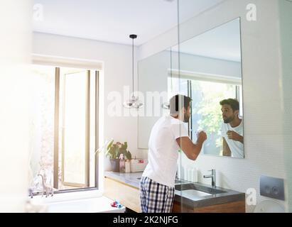 Zweimal am Tag hält den Zahnarzt fern. Eine kurze Aufnahme eines hübschen Mannes, der zu Hause in den Spiegel schaut und seinen Mund im Badezimmer ausspült. Stockfoto