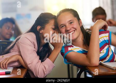 Kannst du ein Geheimnis bewahren? Aufnahme einer jungen Schülerin, die ihrem Freund in der Klasse ein Geheimnis flüstert. Stockfoto